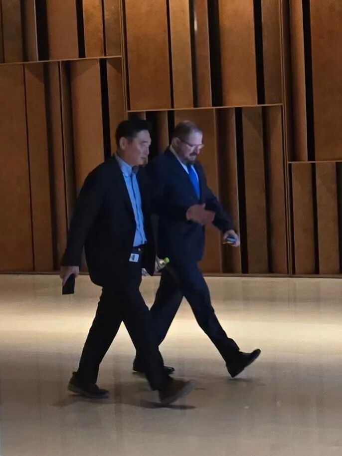 兩個穿西裝的男人一起走在現代走廊上，走廊里有木質墻板。